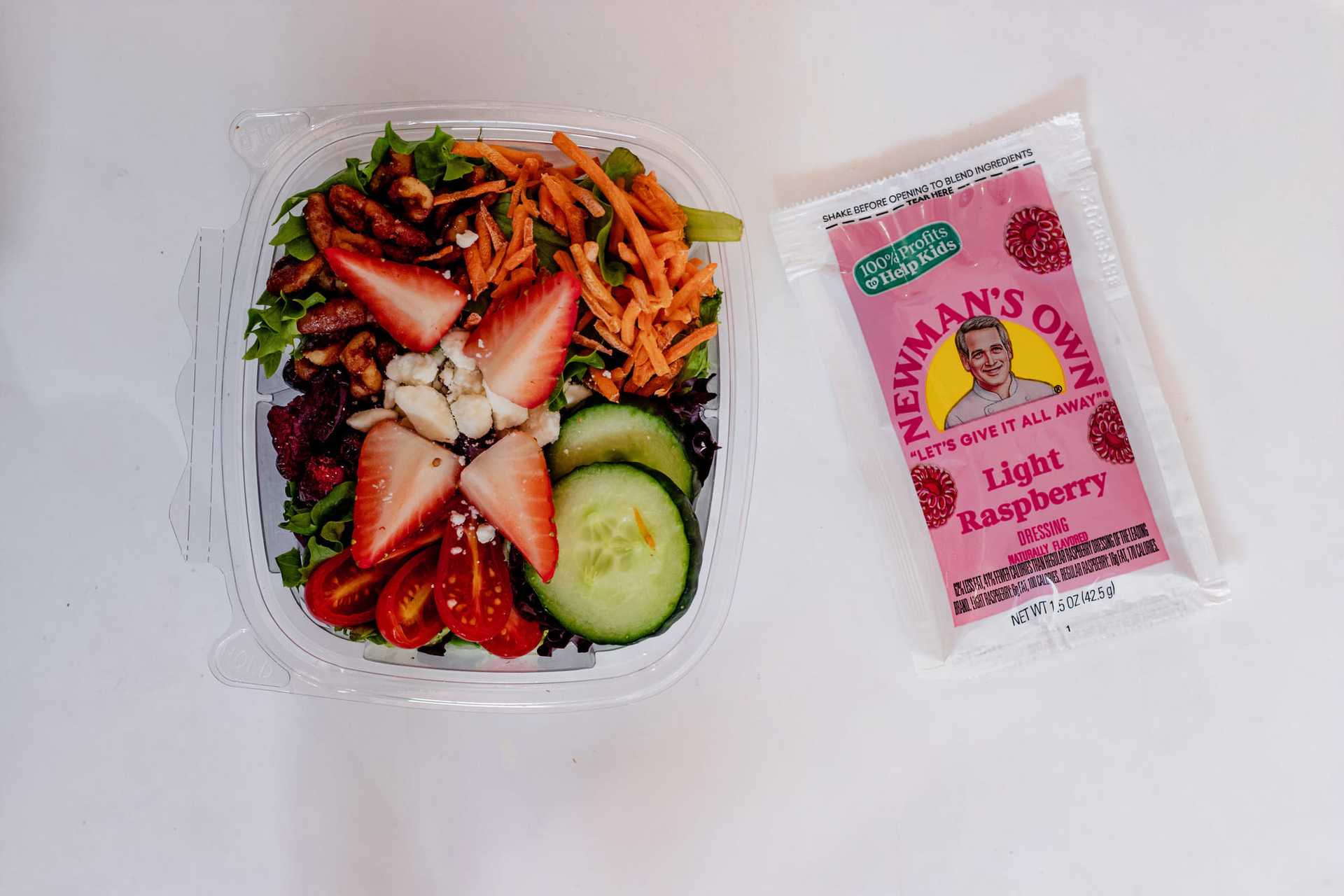 Fresh salad with strawberries, tomatoes, and dressing packet on the side.