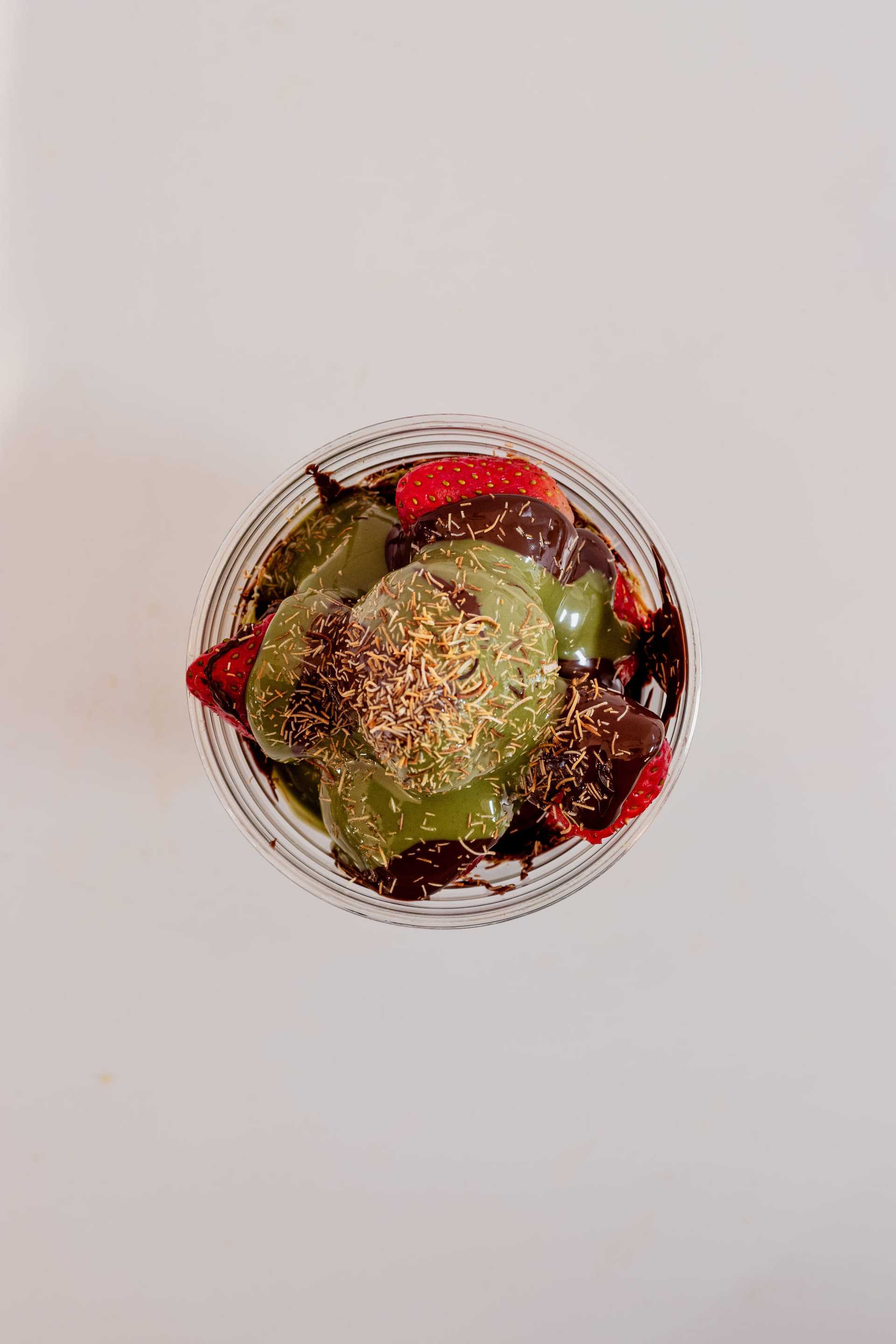 Aerial view of a dessert with strawberries, chocolate, and green jelly in a glass bowl.