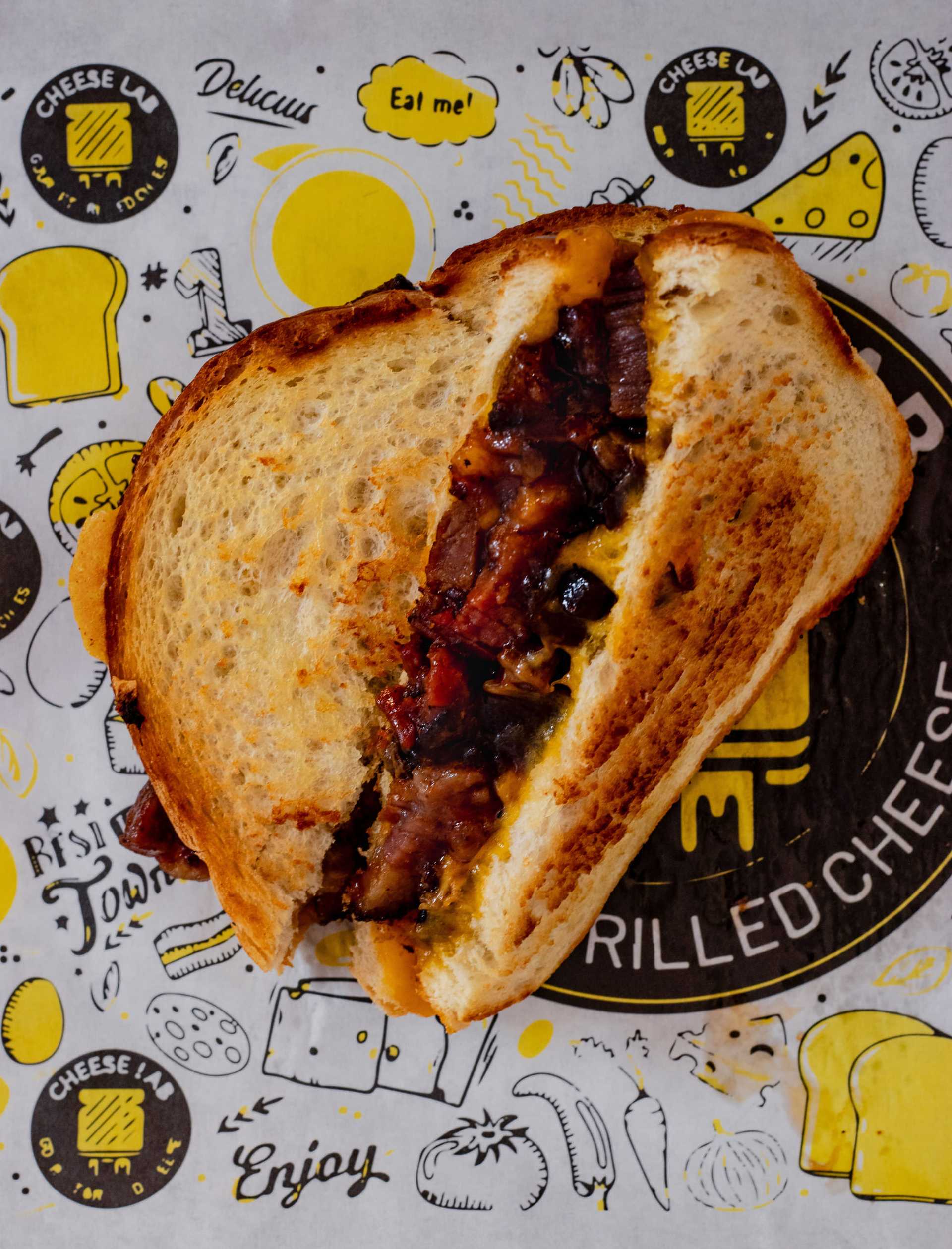 Grilled cheese sandwich with caramelized onions on themed paper wrapping.