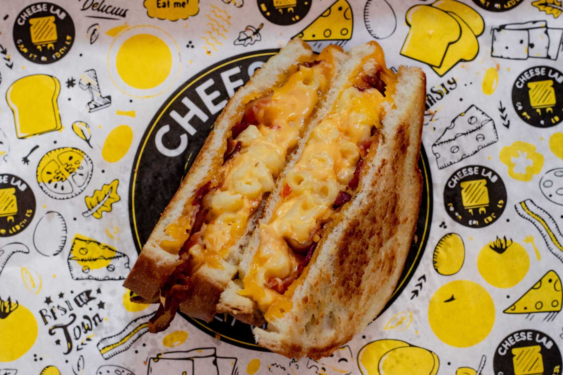 Grilled cheese sandwich with macaroni on colorful, cheese-themed paper.