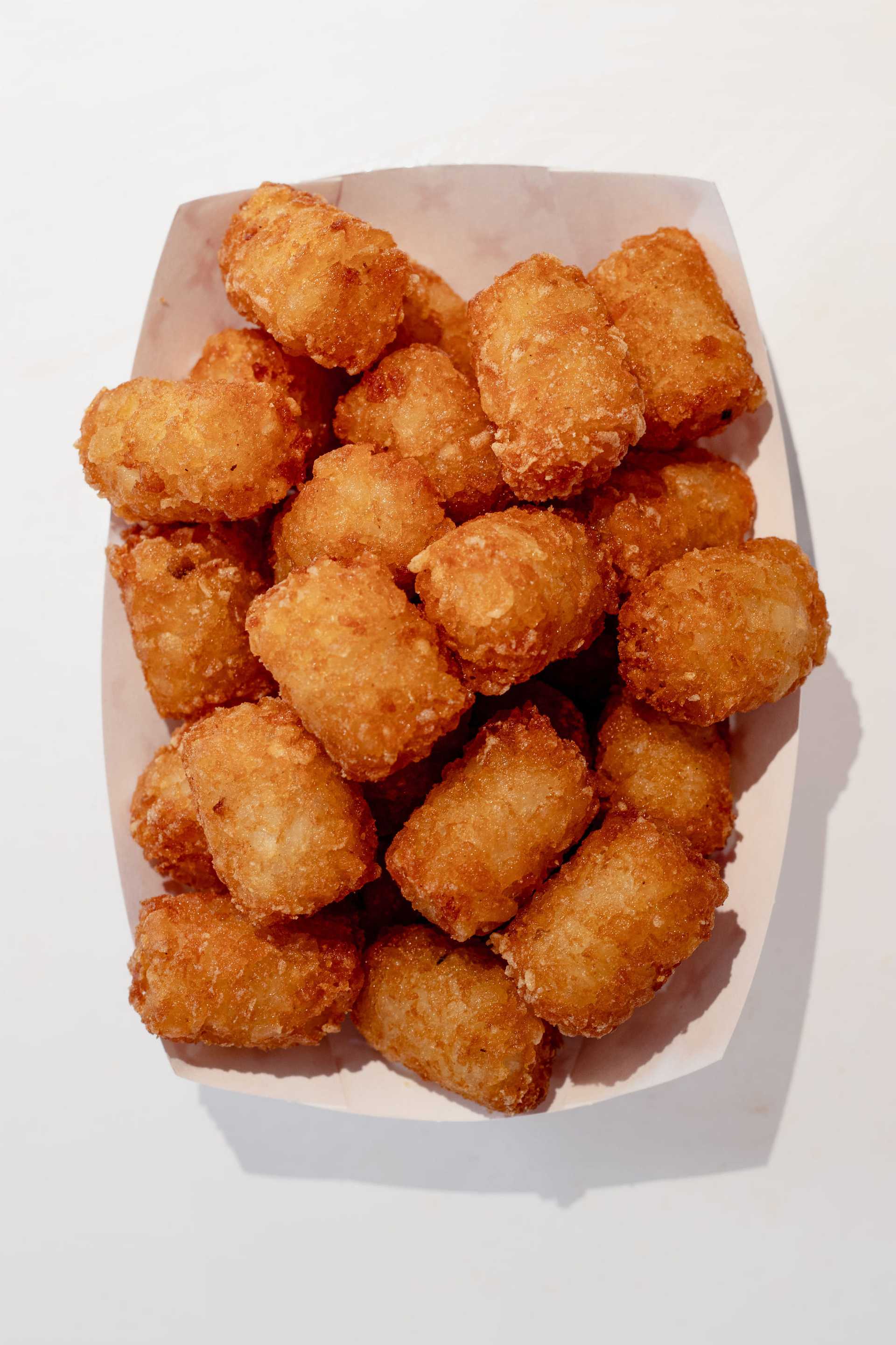 Crispy golden tater tots in a paper tray on a white background.