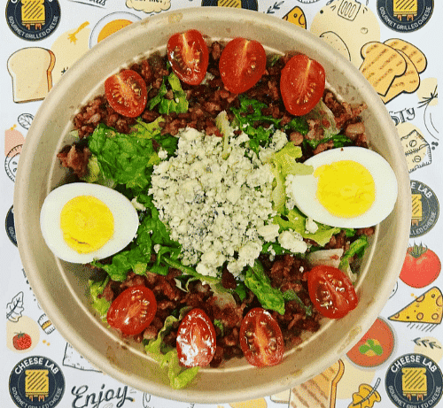 A bowl of salad with eggs, tomatoes, lettuce, and crumbled cheese.
